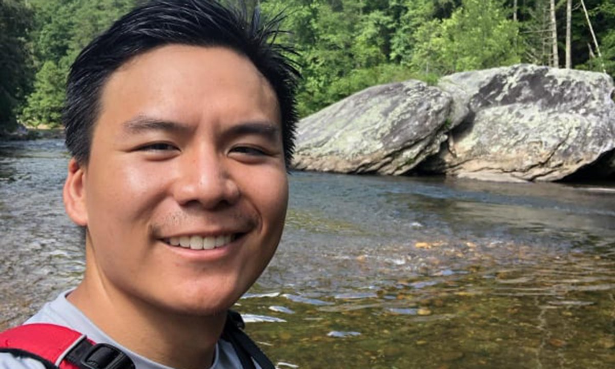 Adult man smiling in front of a small river.