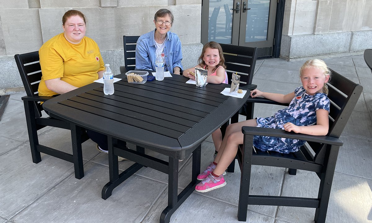 An image of Science Museum guests eating a snack at black recycled plastic tables. There are two adults and two children seated.