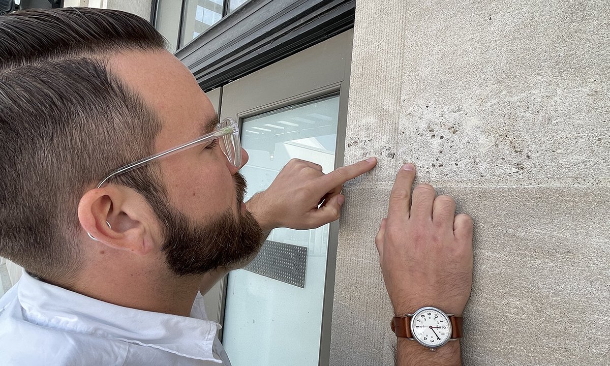 Man in white shirt wearing glasses looking at a wall and using his finger to feel for fossils.