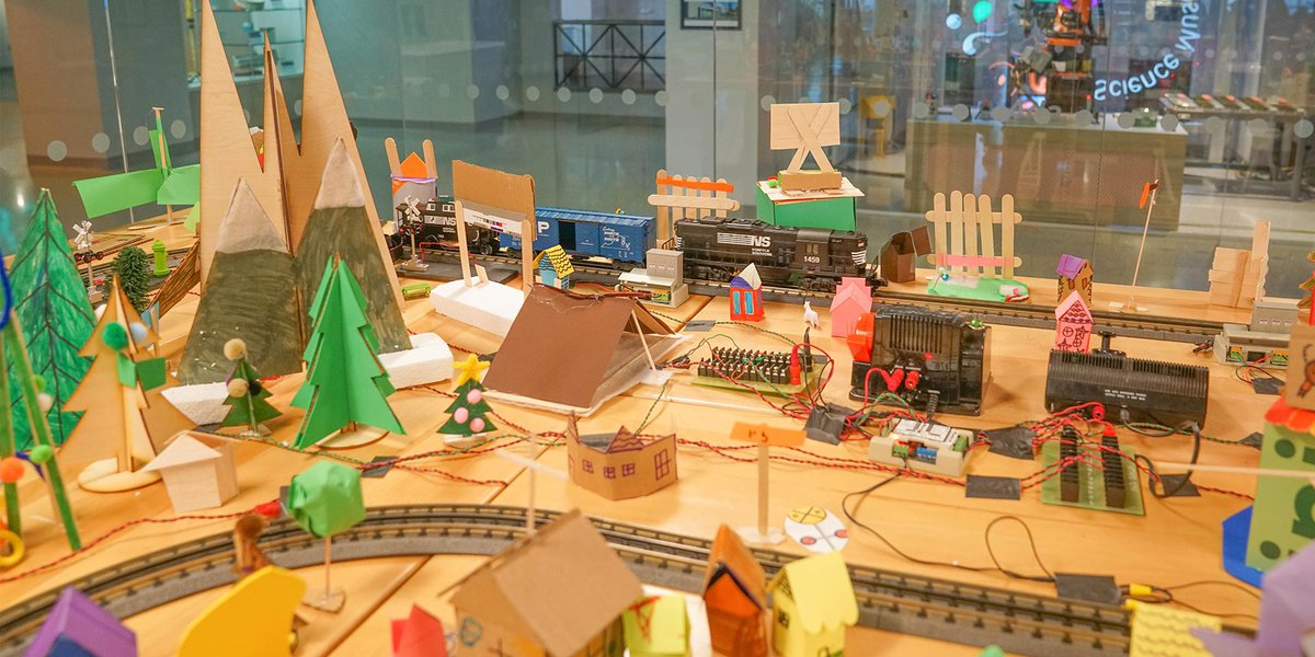 Toy train on traintracks going through colorful cardboard town. This set up is in The Forge.