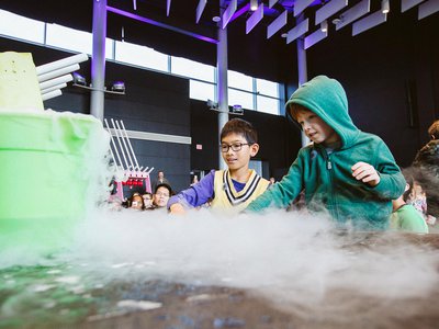 Children watching the supercool demo with awe as liquid nitrogen escapes from a green bucket.